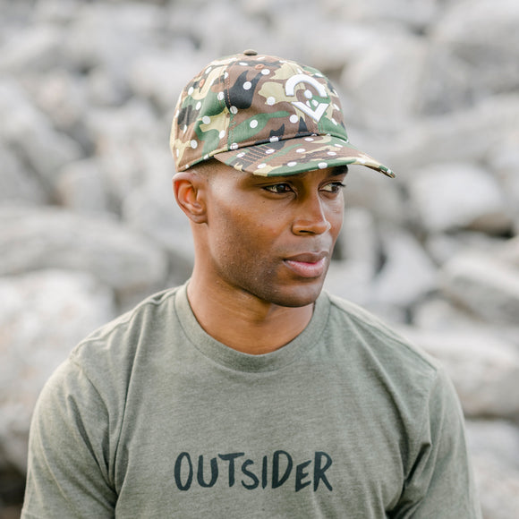 Outsider camo hat with white dots and embroidered logo modeled on a man